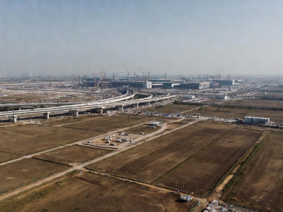 10 Things to Consider Before Buying Land Near Jewar Airport- A wide-angle landscape view of the developing region around Jewar Airport in NCR, India. In the foreground, open land parcels with boundary markers and survey poles. In the background, large airport construction with cranes, runways, and expressway connectivity. Investors and real estate professionals reviewing site maps on a tablet. Bright daylight, realistic photography style, ultra-detailed, 16:9 ratio, cinematic composition, modern infrastructure blending with rural land.